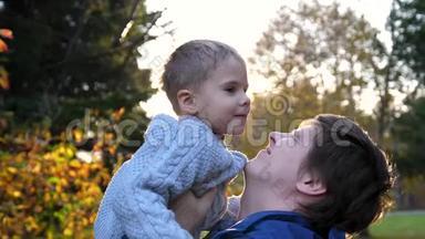 一个年轻的父亲和一个孩子玩，把他抱在怀里，吐了出来。 太阳`阳光透过孩子。 笑声